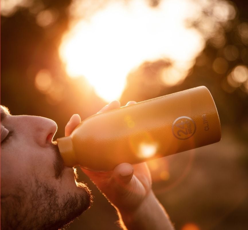 Homem a beber água de uma garrafa térmica 24Bottles ao pôr do sol, transmitindo a sensação de aventura, bem-estar e hidratação em qualquer momento do dia.